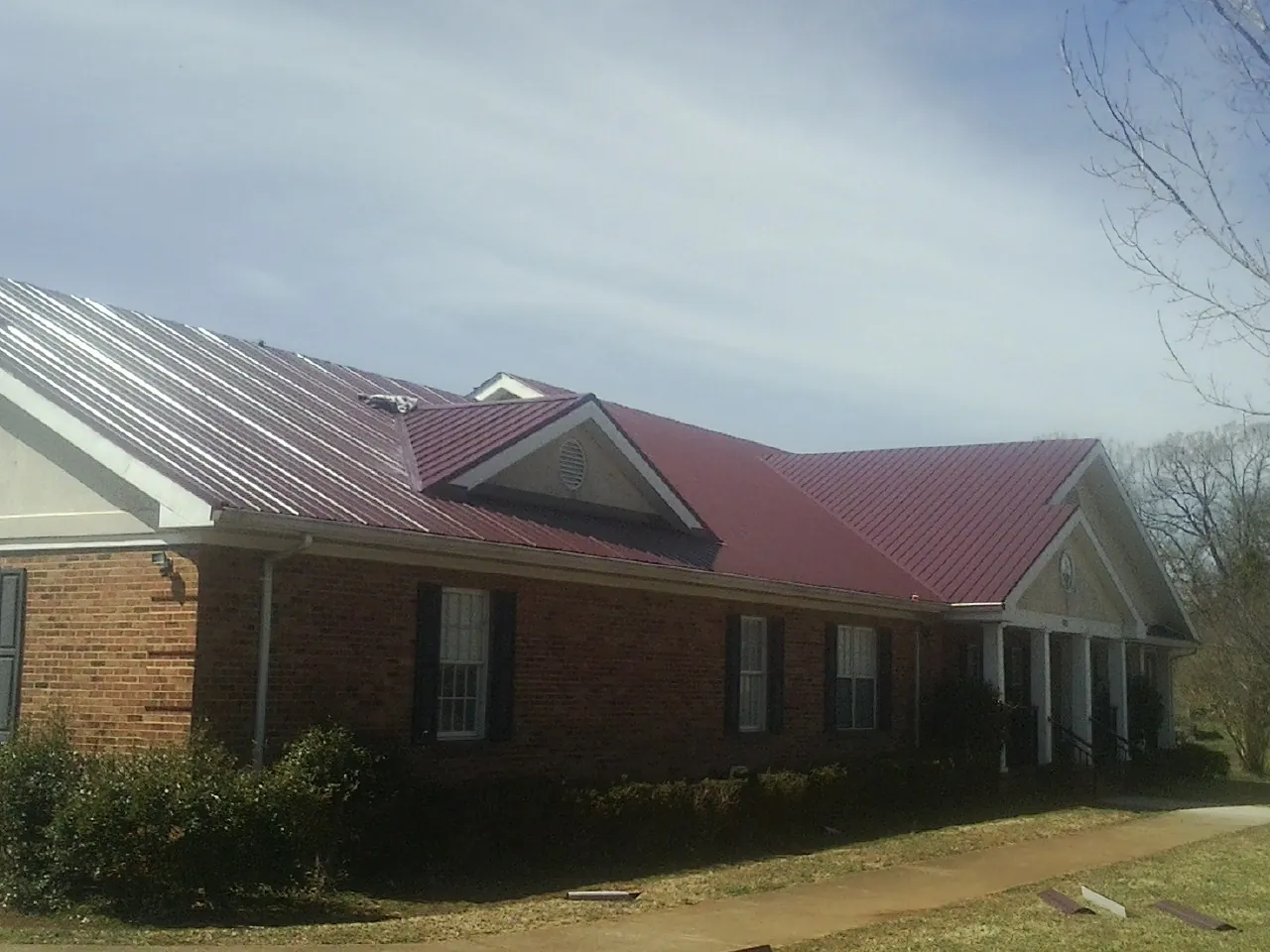 Red metal roof with gabled entries on a long brick building, from a Hail Damage Roof Repair job in Idabel