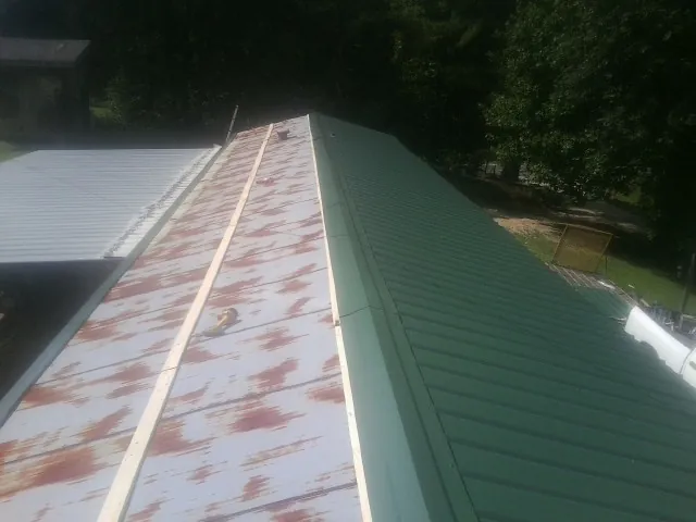 Old rusted panels beside newly installed green metal roofing — Wind Damage Roof Repair by Roofing Brothers in Idabel