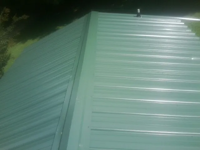 New green metal panels meeting at the ridge of a roof — Flat Roof Repair work by our crew in Idabel