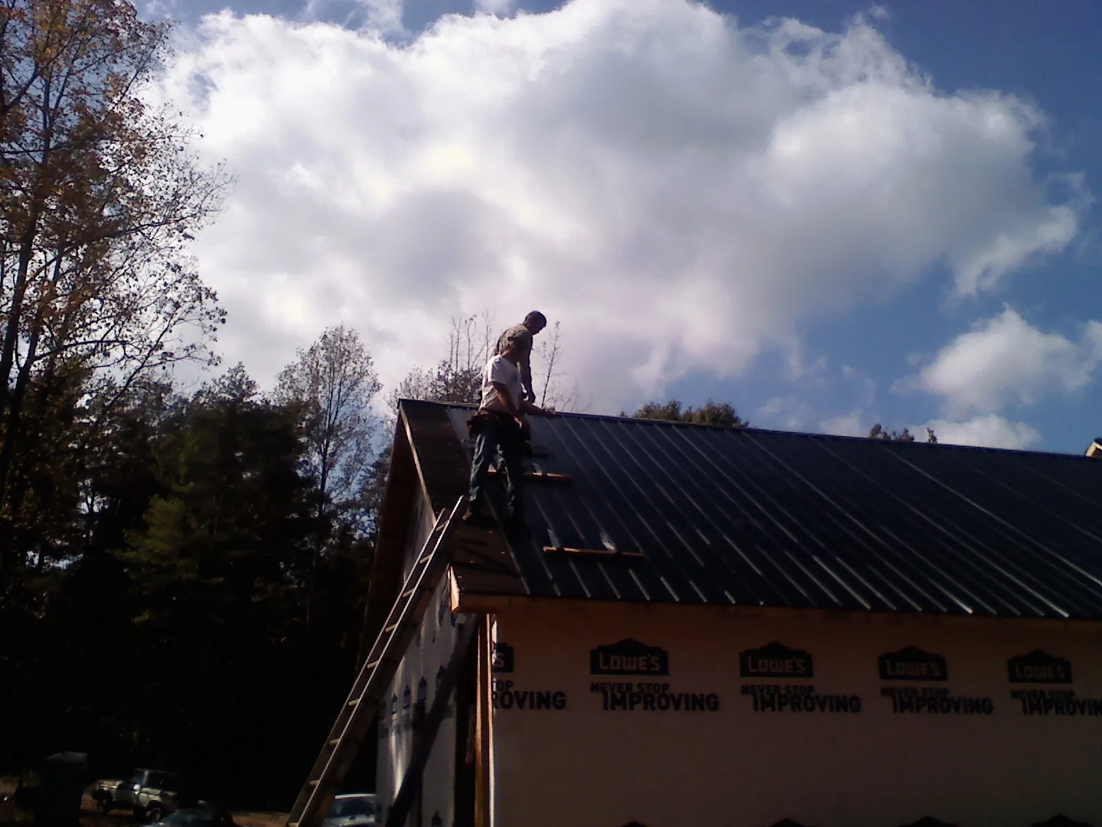 Roofer fastening dark metal panels high against a cloudy sky, from a Roof Inspection job in Idabel