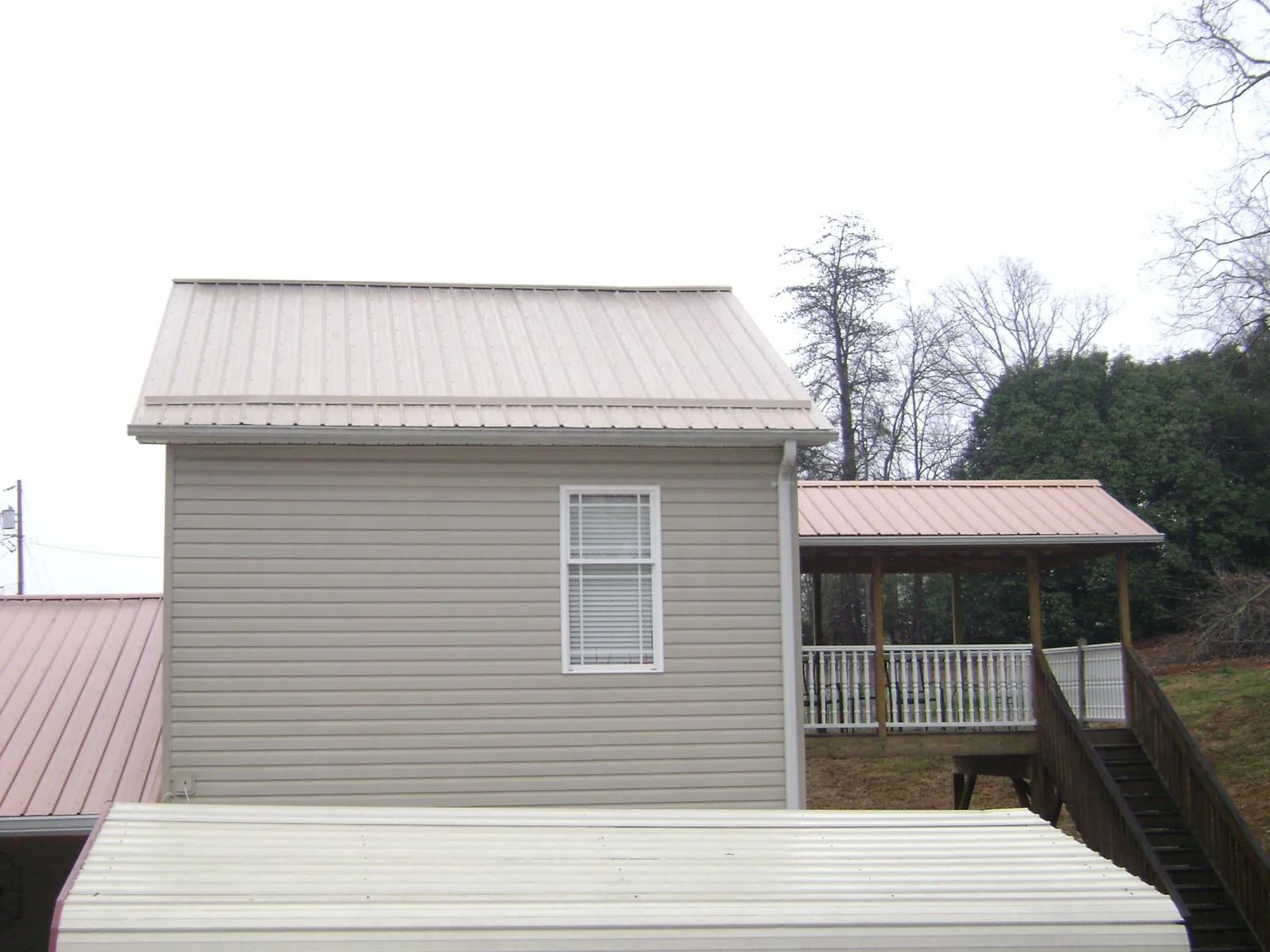 Tan metal roofs on a two story addition and attached porch, from a Roof Replacement job in Idabel